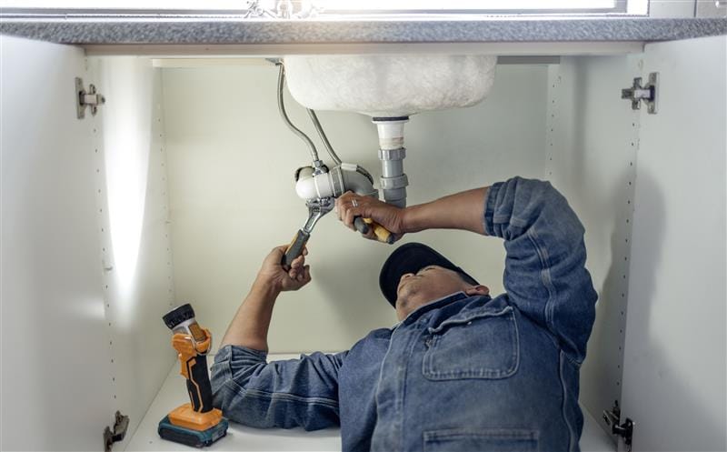 Plumber repairing pipes beneath a bathroom sink in Sanford