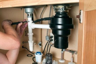 Plumber repairing a garbage disposal beneath a kitchen sink in Sanford