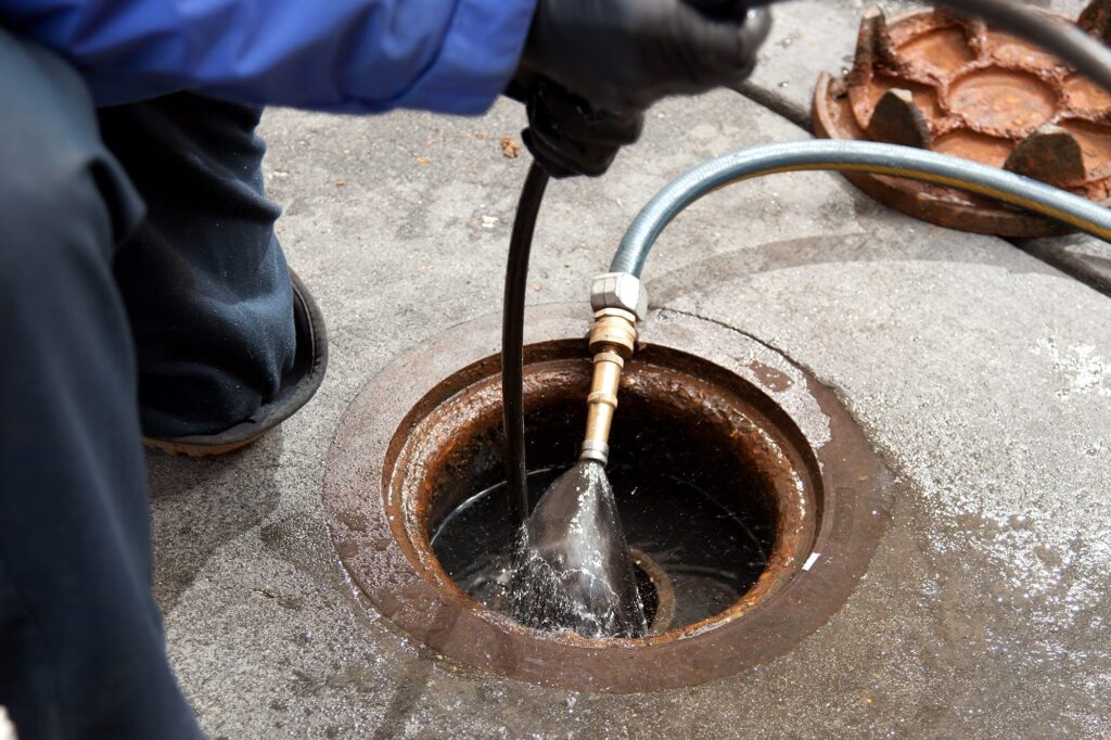 Plumber hydro jetting a sewer line through a manhole in Sanford