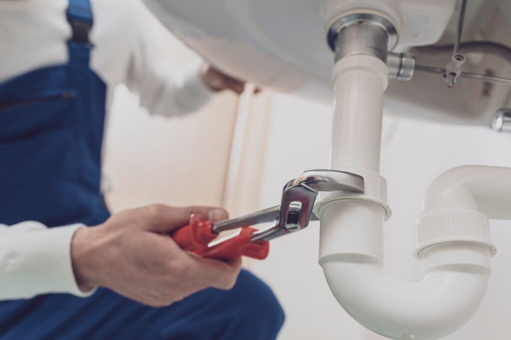 Plumber repairing a white drain pipe beneath a sink in Sanford