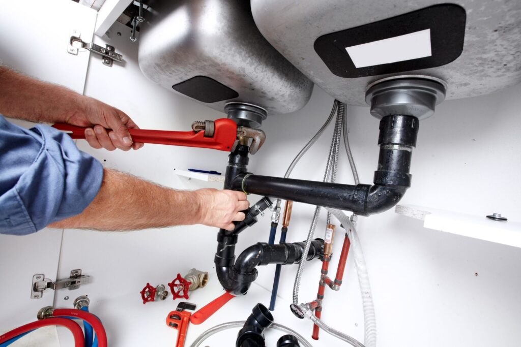 Plumber repairing drain pipes beneath a kitchen sink in Sanford
